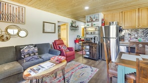 A cozy living room with a sofa, armchair, and coffee table, a kitchen with wooden cabinets and appliances, and a dining area with a table and chairs. - Ski-in Red River Retreat: Balcony, Mountain Views! (Red River)