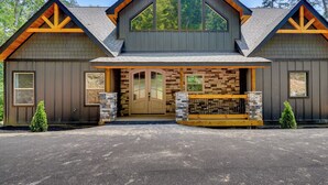 A two-story log cabin with a stone facade, large windows, and a wooden porch.