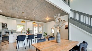 A modern kitchen with white cabinets, a wooden dining table, and a staircase.