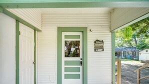A white door with green trim and a welcome sign, a wooden porch, and a doormat. - New Braunfels Vacation Rental on Lake Dunlap! (New Braunfels)