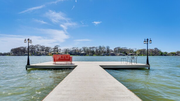 A concrete pier extending into a body of water, with a red bench and two street lamps on either side. - New Braunfels Vacation Rental on Lake Dunlap! (New Braunfels)