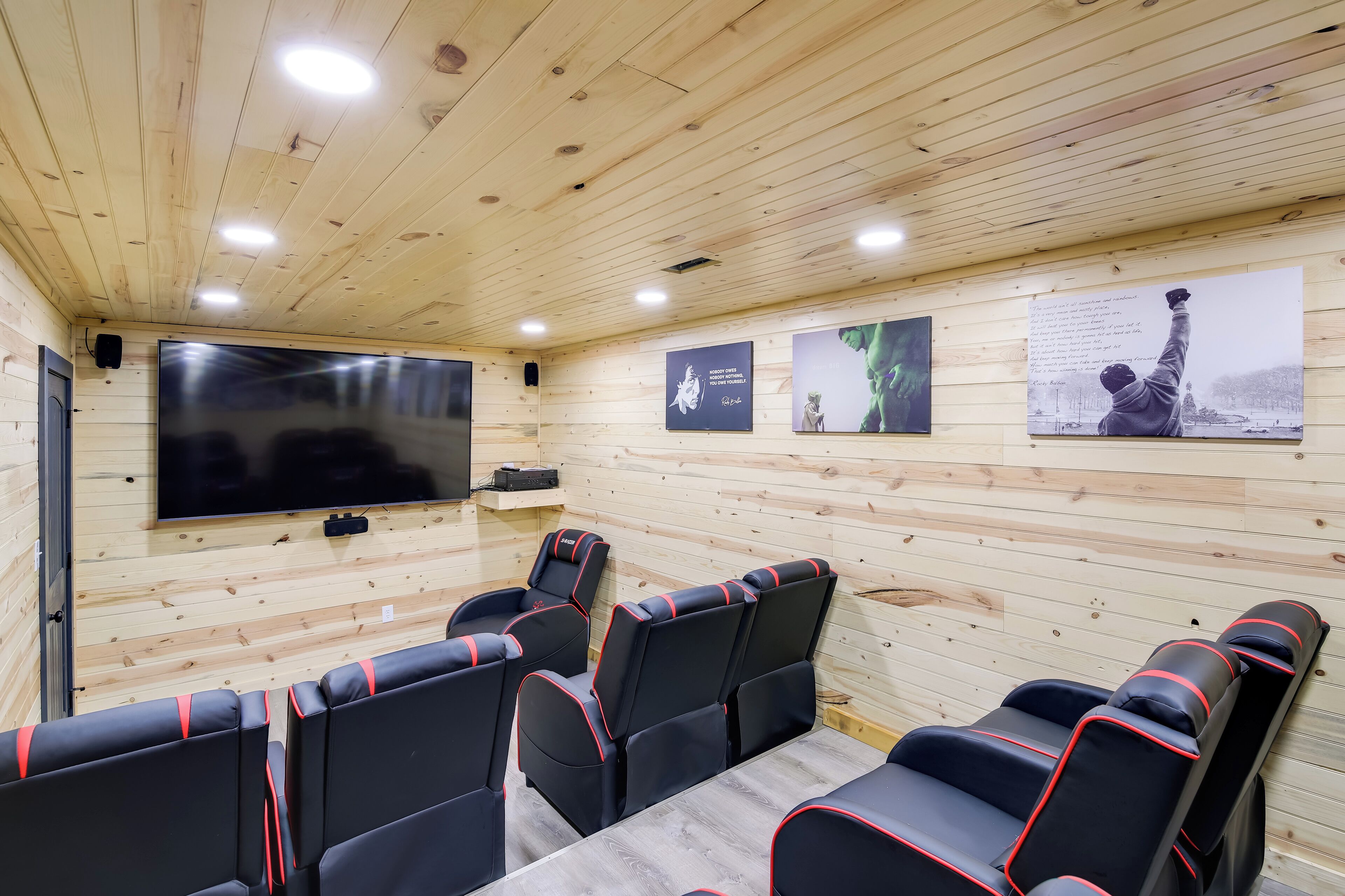 Una habitación con paneles de madera, televisor de pantalla plana y varios sillones tapizados en negro y rojo.