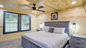 A wooden-paneled bedroom with a bed, nightstands, and a ceiling fan.