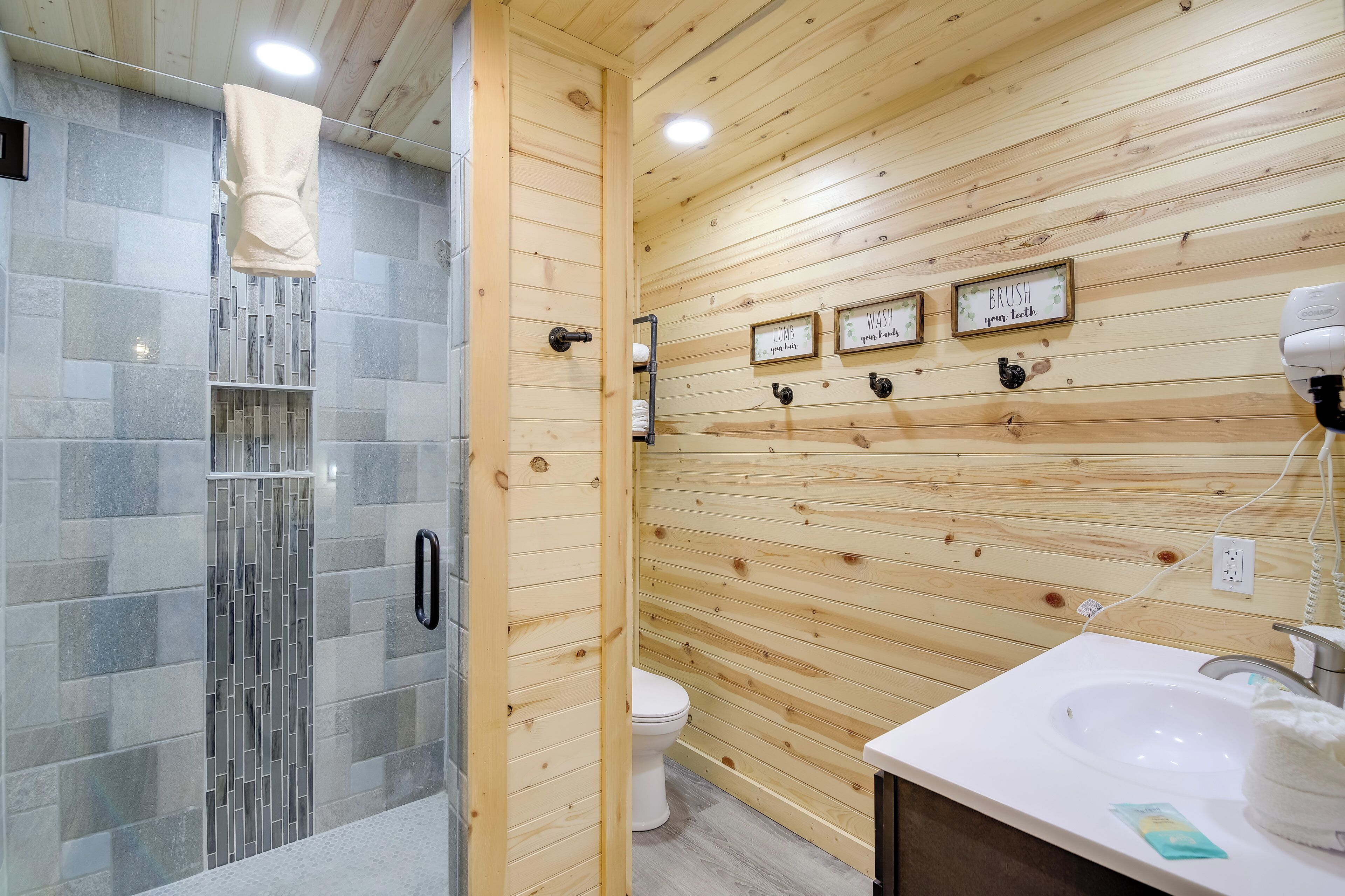 A wooden-paneled bathroom with a glass shower enclosure, a toilet, and a sink with a towel hanging on the wall.