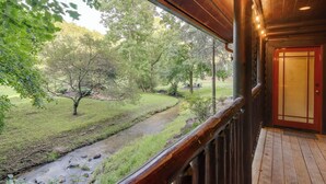 Een houten veranda met uitzicht op een grasveld en een beek.