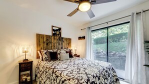 A bedroom with a large bed, a ceiling fan, a nightstand with a lamp, and a view of a garden through a sliding door. - Sevierville Condo w/ Balcony + Pool Access! (Sevierville)