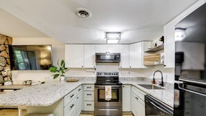 A modern kitchen with white cabinets, a granite countertop, stainless steel appliances, and a built-in oven. - Sevierville Condo w/ Balcony + Pool Access! (Sevierville)