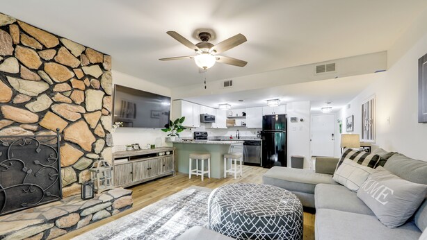 A modern living room with a stone accent wall, a ceiling fan, and a grey sofa with 'HOME' pillows. - Sevierville Condo w/ Balcony + Pool Access! (Sevierville)