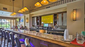 A bar area with a long counter, multiple bar stools, and a television screen. - Palm Desert Resort Country Club Vacation Rental! (Palm Desert)