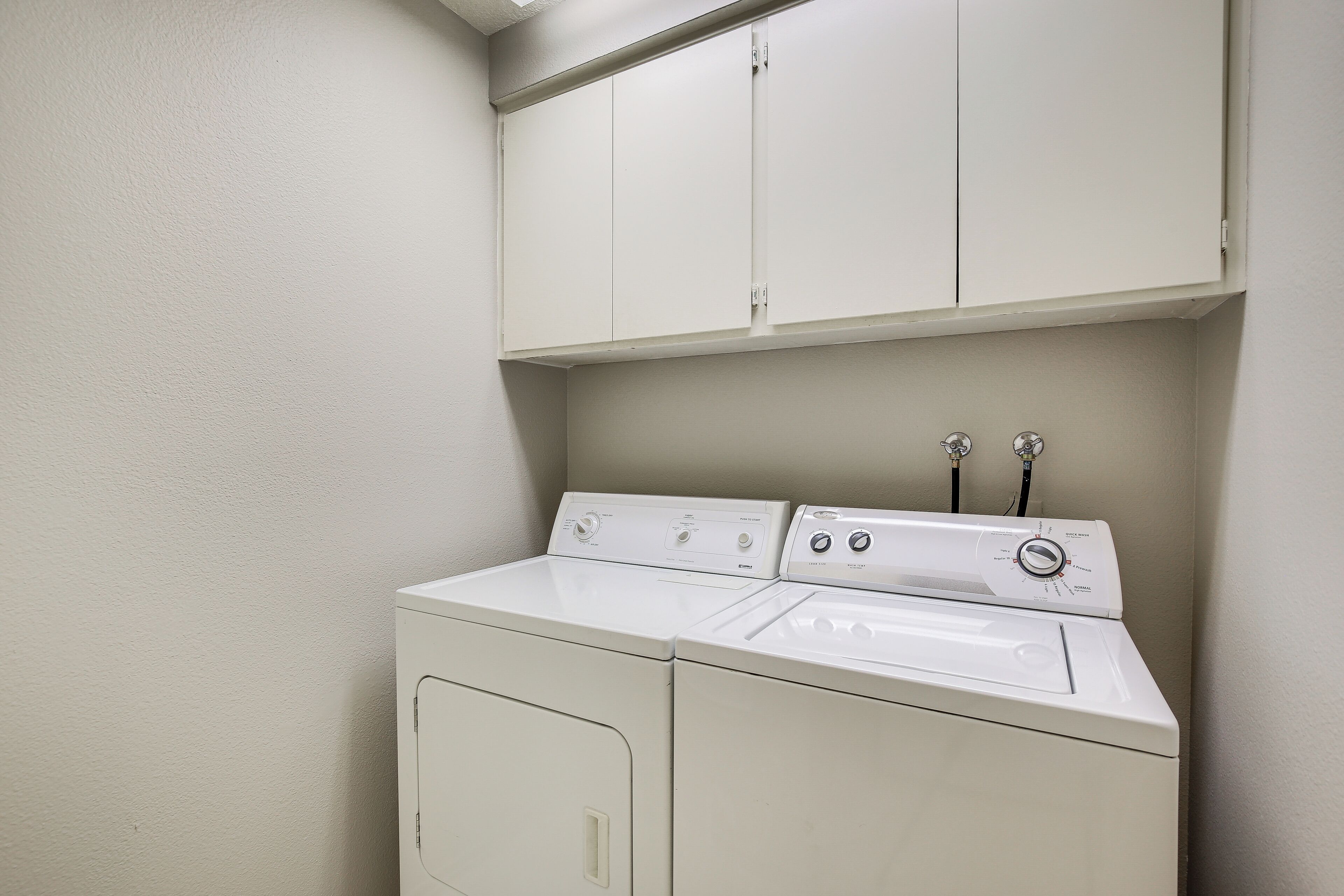 A laundry room with a front-loading washer and dryer, a cabinet above the dryer, and a wall-mounted towel rack.