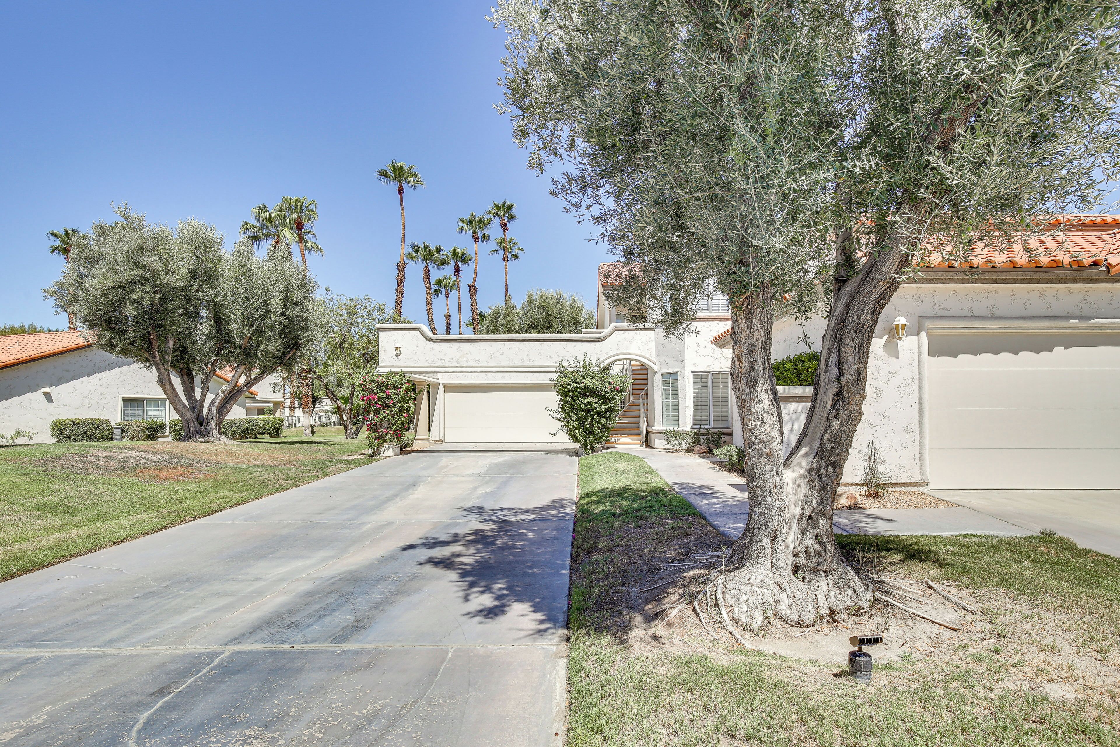 A residential driveway with a tree, a well-maintained lawn, and a house with a garage.