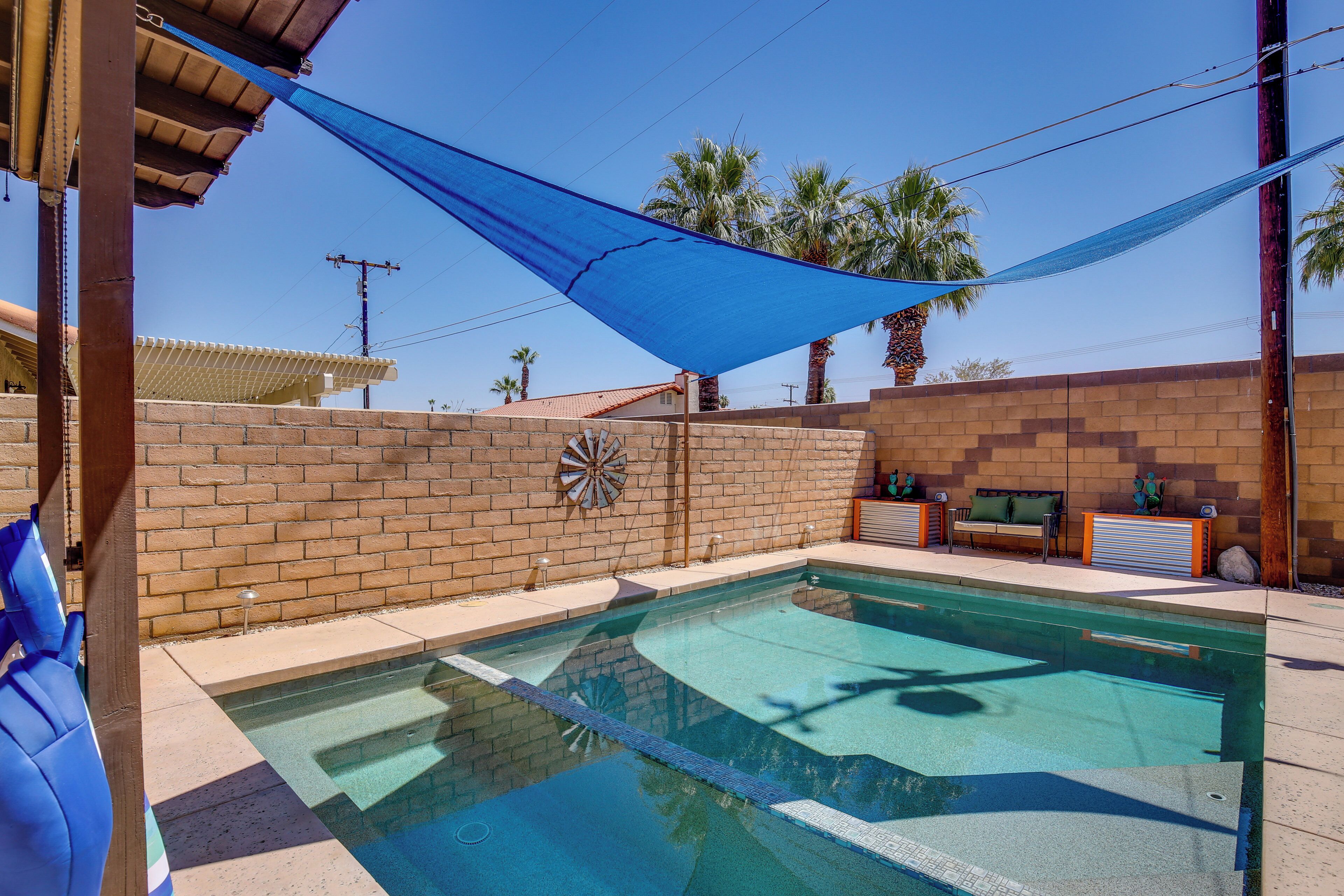 Una piscina con un telo parasole blu, un muro in mattoni e un bersaglio da freccette.