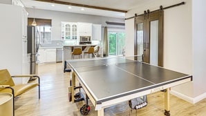 A spacious room with a ping pong table, wooden flooring, and a kitchen area in the background. - Palm Desert Home w/ Pool, Near Shops on El Paseo! (Palm Desert)