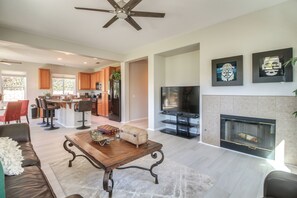 A spacious living room with a fireplace, a television, and a kitchen area in the background. - 2 Mi to Coachella: Indio Home w/ Outdoor Oasis (Indio)