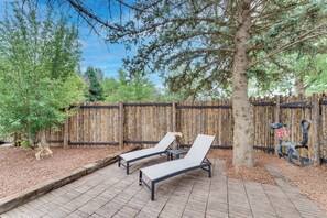Two lounge chairs on a wooden deck with a wooden fence and trees in the background.