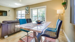 A modern living room with a sofa, a dining table with chairs, a TV, and a window with a view of trees. - North Lauderdale Vacation Rental: 8 Mi to Beach! (North Lauderdale)