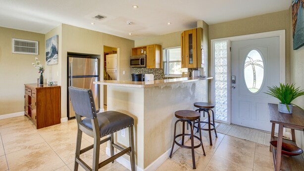 A kitchen with a central island, bar stools, a refrigerator, microwave, and wooden cabinets. - North Lauderdale Vacation Rental: 8 Mi to Beach! (North Lauderdale)