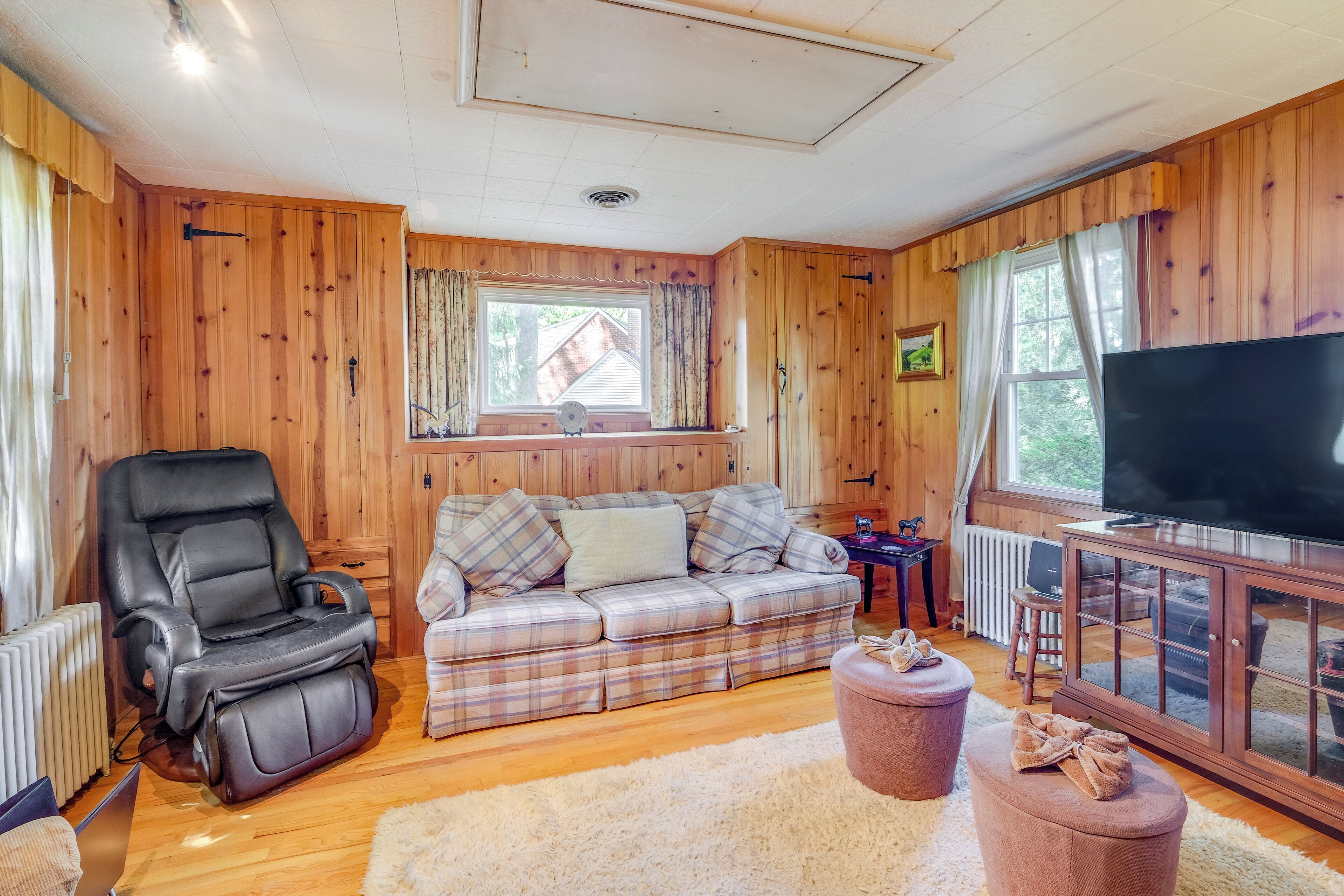 Een gezellige woonkamer met een massagestoel, een geruite bank, een flatscreen televisie en een houten kast.