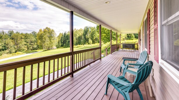 Une véranda couverte avec des balustrades en bois, deux chaises vertes et une vue sur un paysage verdoyant.