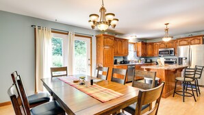 Une cuisine moderne avec des meubles en bois, des appareils électroménagers en acier inoxydable et un coin repas comprenant une table et des chaises en bois.