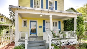 Une maison jaune avec un porche, des balustrades blanches et une porte bleue.