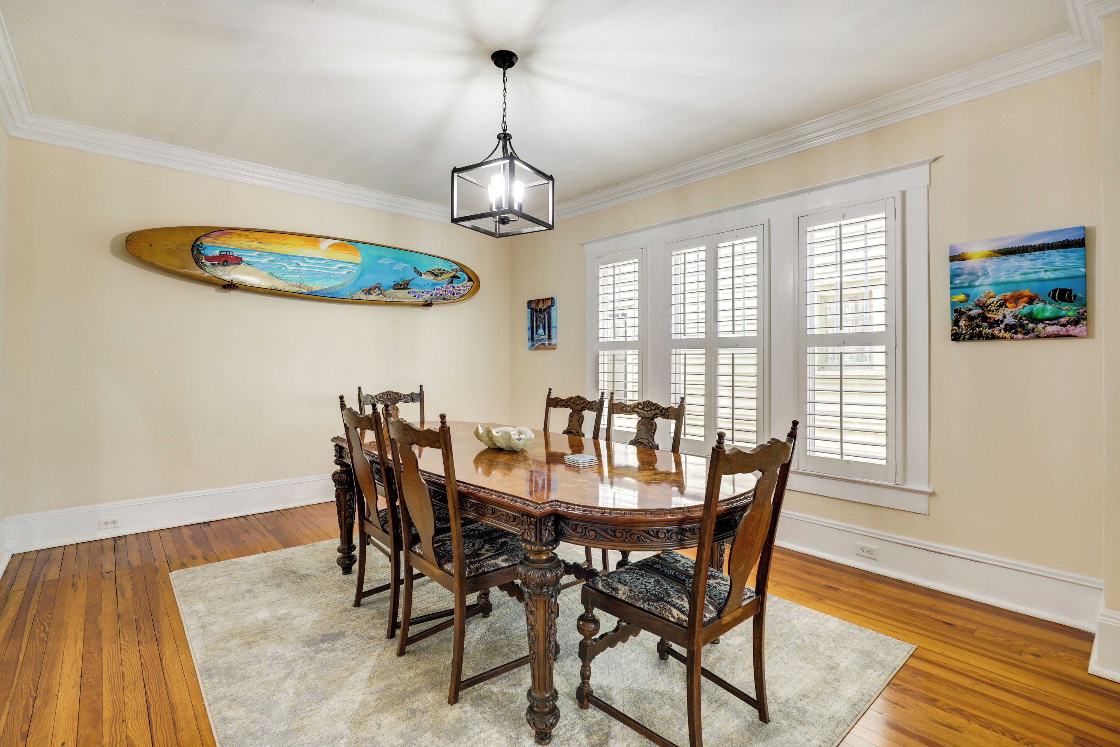 A dining room with a wooden table and chairs, a chandelier, and artwork on the walls.