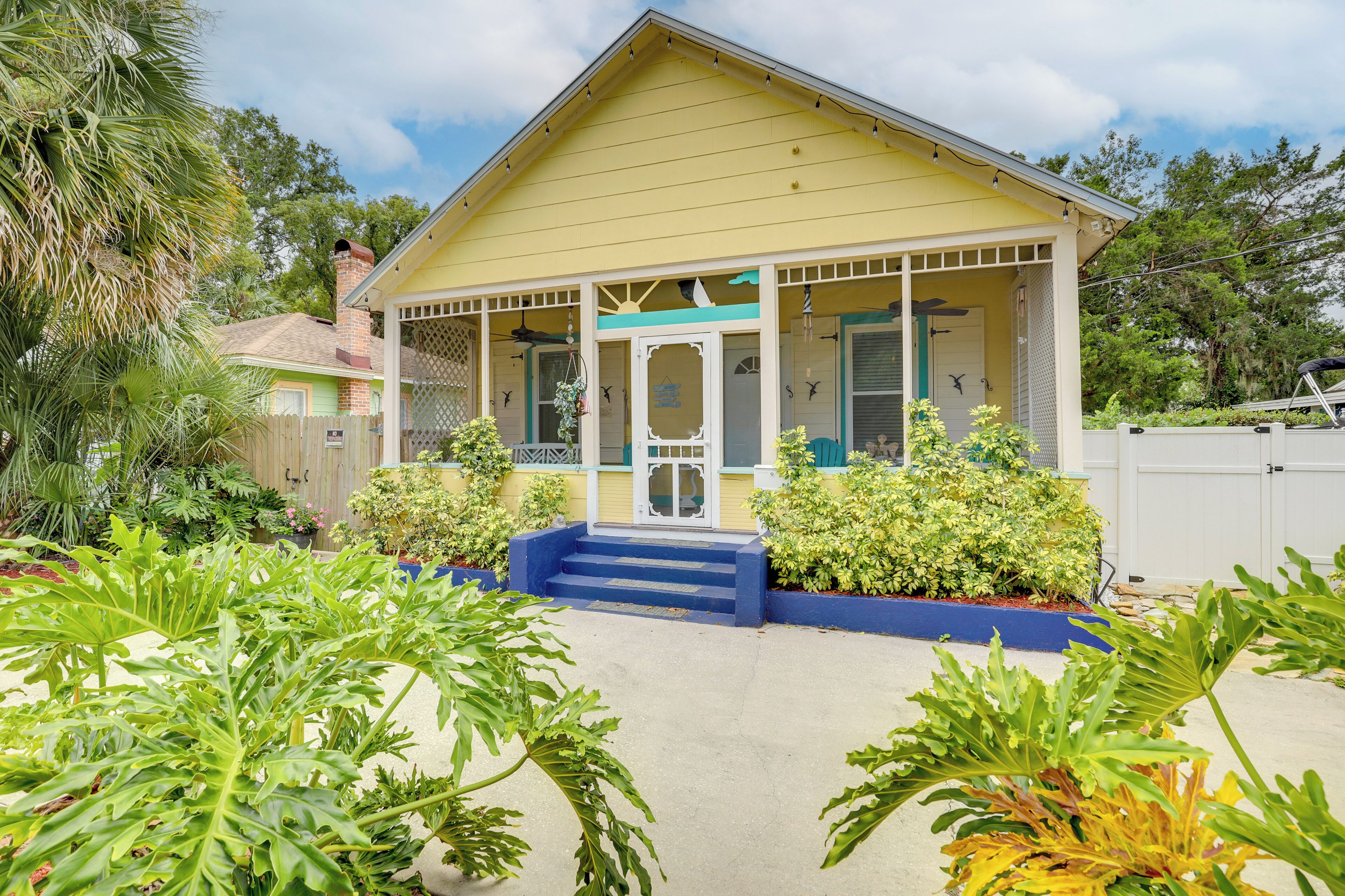 A yellow house with a porch, surrounded by greenery.