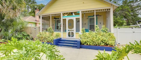 A yellow house with a porch, surrounded by greenery.