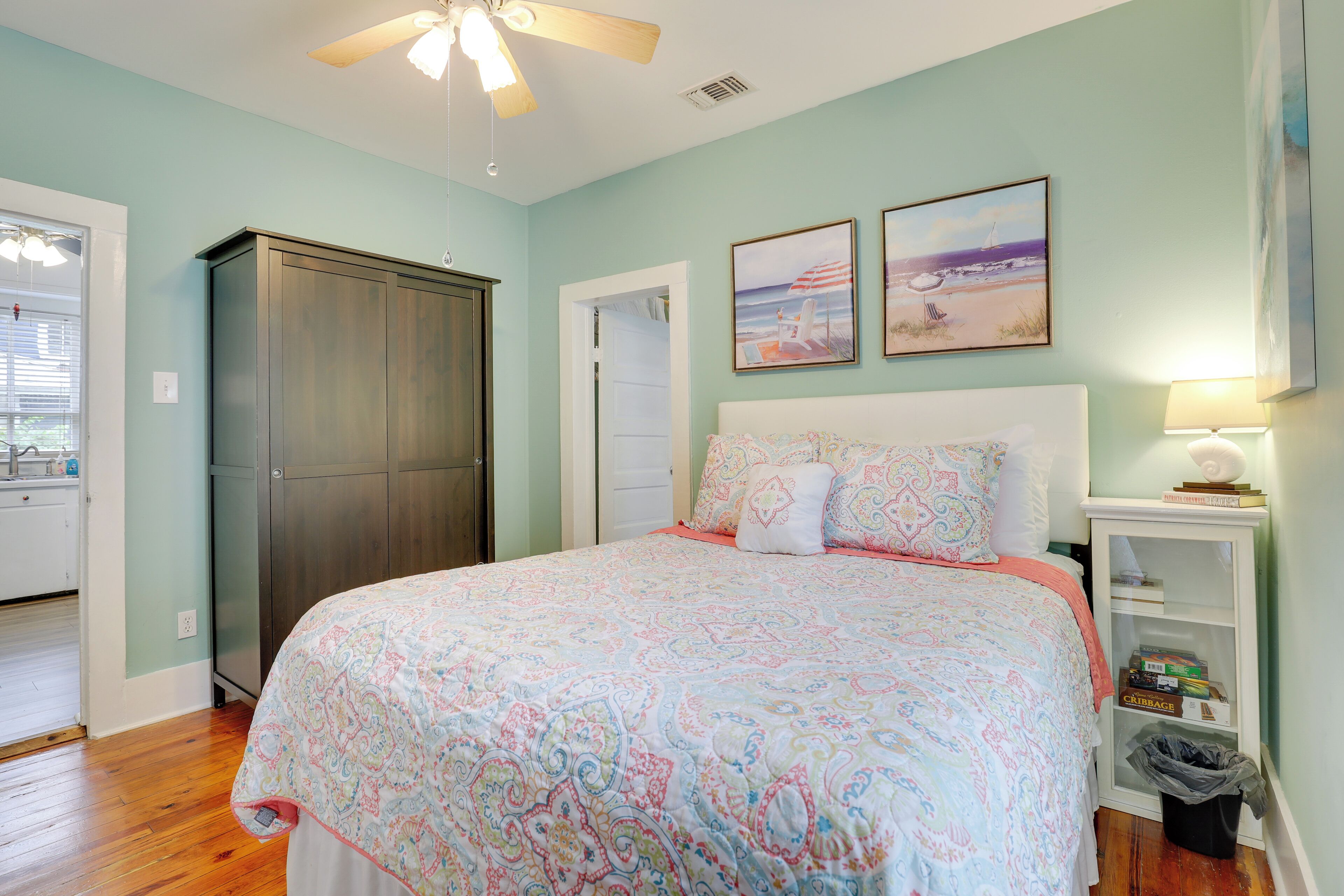 A bedroom with a bed, a wardrobe, a nightstand, and a wall with two framed pictures.