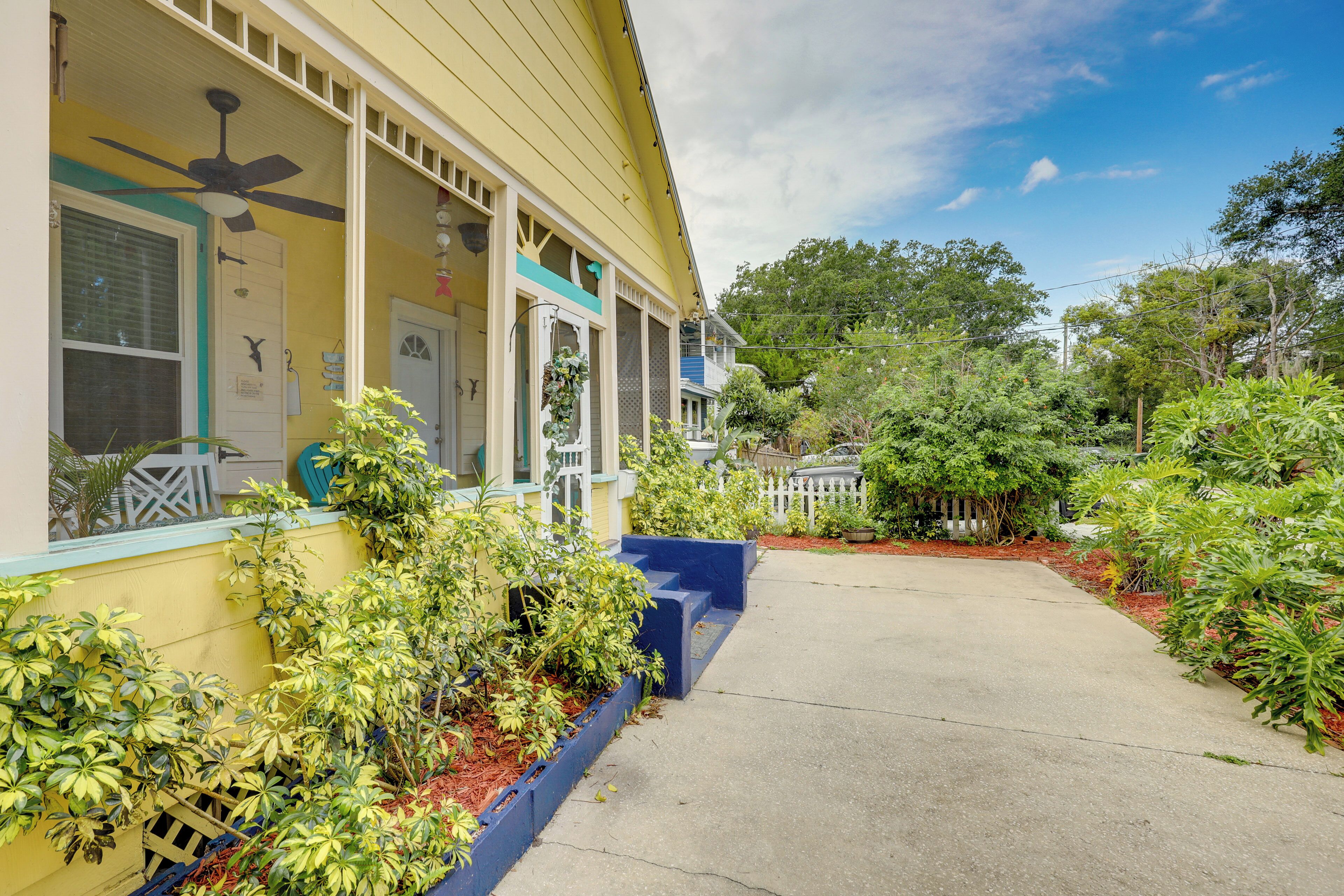A yellow building with a covered porch, a ceiling fan, and a white picket fence.