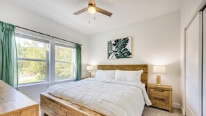 A bedroom with a wooden bed, a nightstand, a ceiling fan, a window with curtains, and a wall-mounted plant. - St Augustine Home < 3 Mi to Historic District! (St. Augustine)