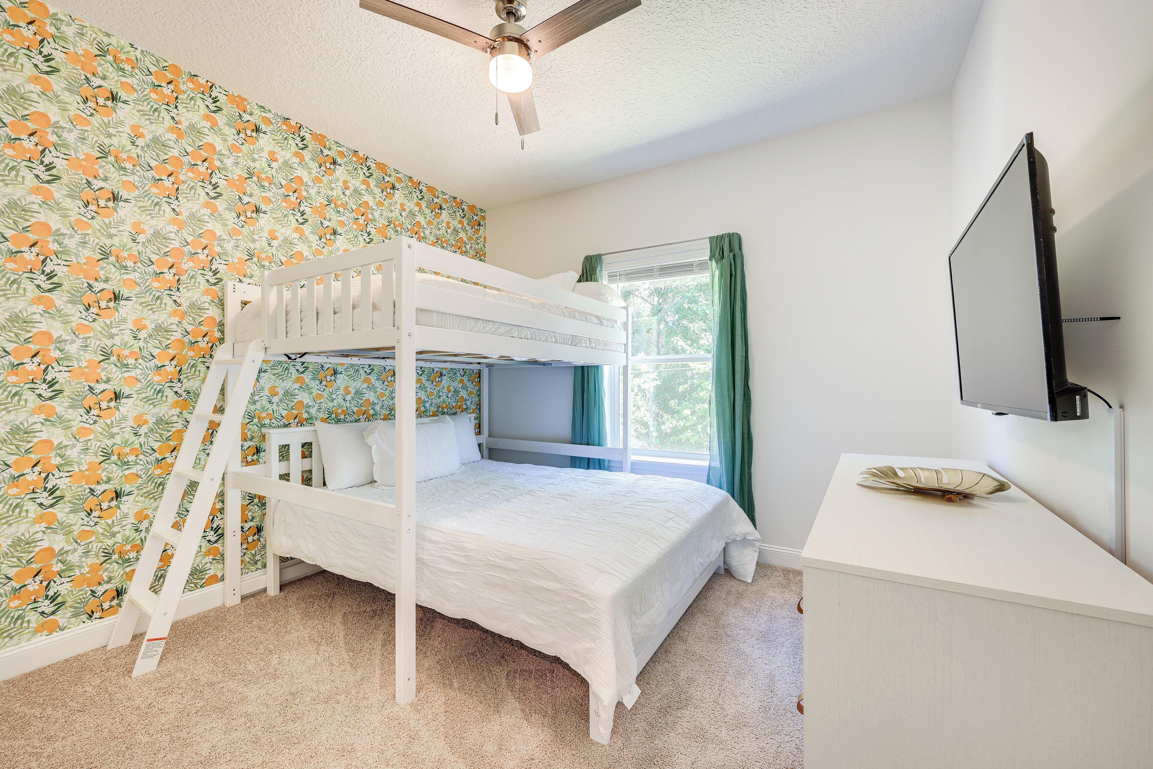 A bunk bed room with a ceiling fan, a desk with a television, and a window with curtains.
