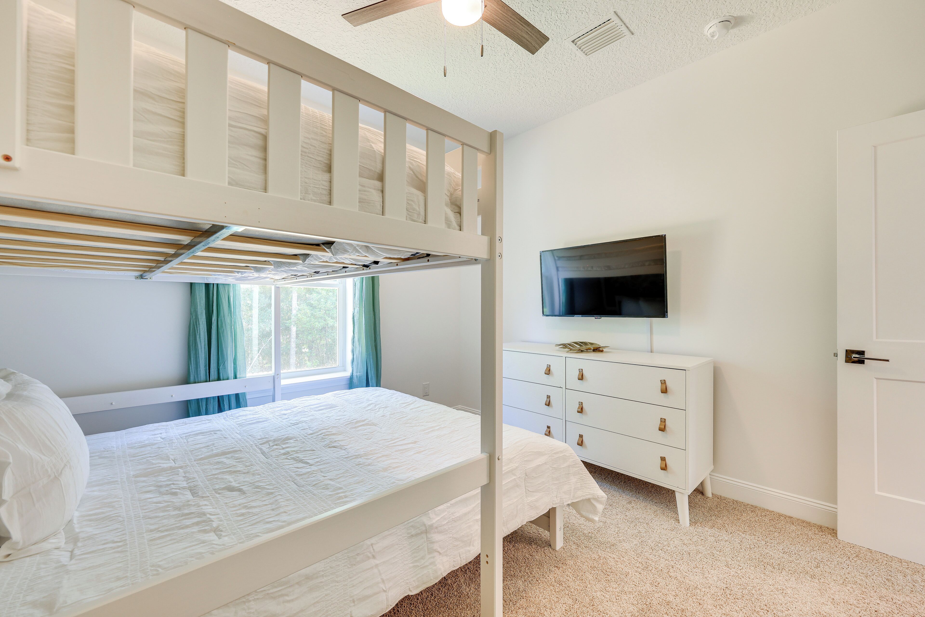 A bedroom with a bunk bed, a dresser, a television, and a window with curtains.