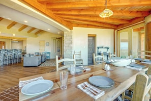 A dining area with a wooden table set for four, surrounded by chairs. A stone wall and a door are visible in the background. - Scenic Santa Fe Vacation Rental w/ Views + Hot Tub (Santa Fe)
