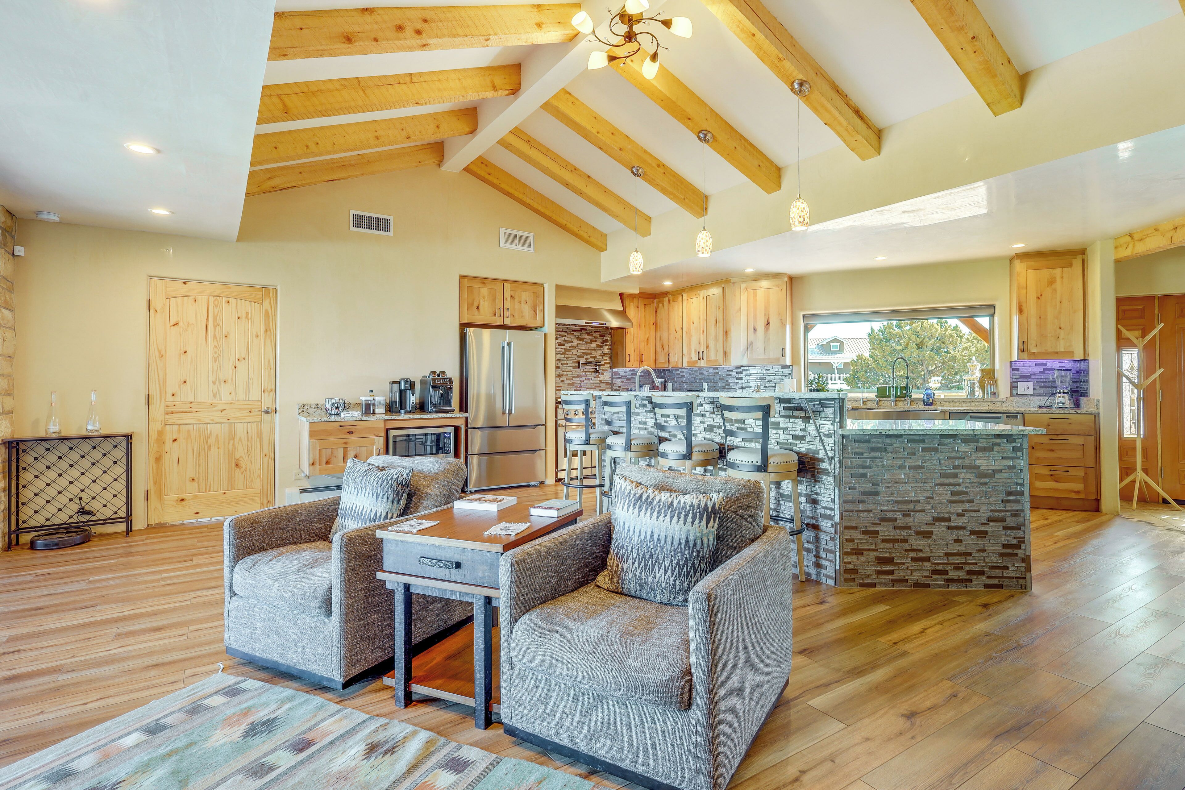 A spacious living area with a wooden ceiling, a kitchen with a stone backsplash, and a dining area with a table and chairs.