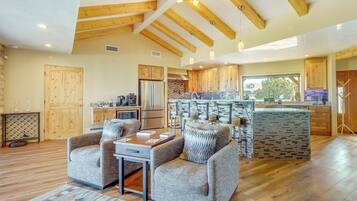 A spacious living area with a wooden ceiling, a kitchen with a stone backsplash, and a dining area with a table and chairs.