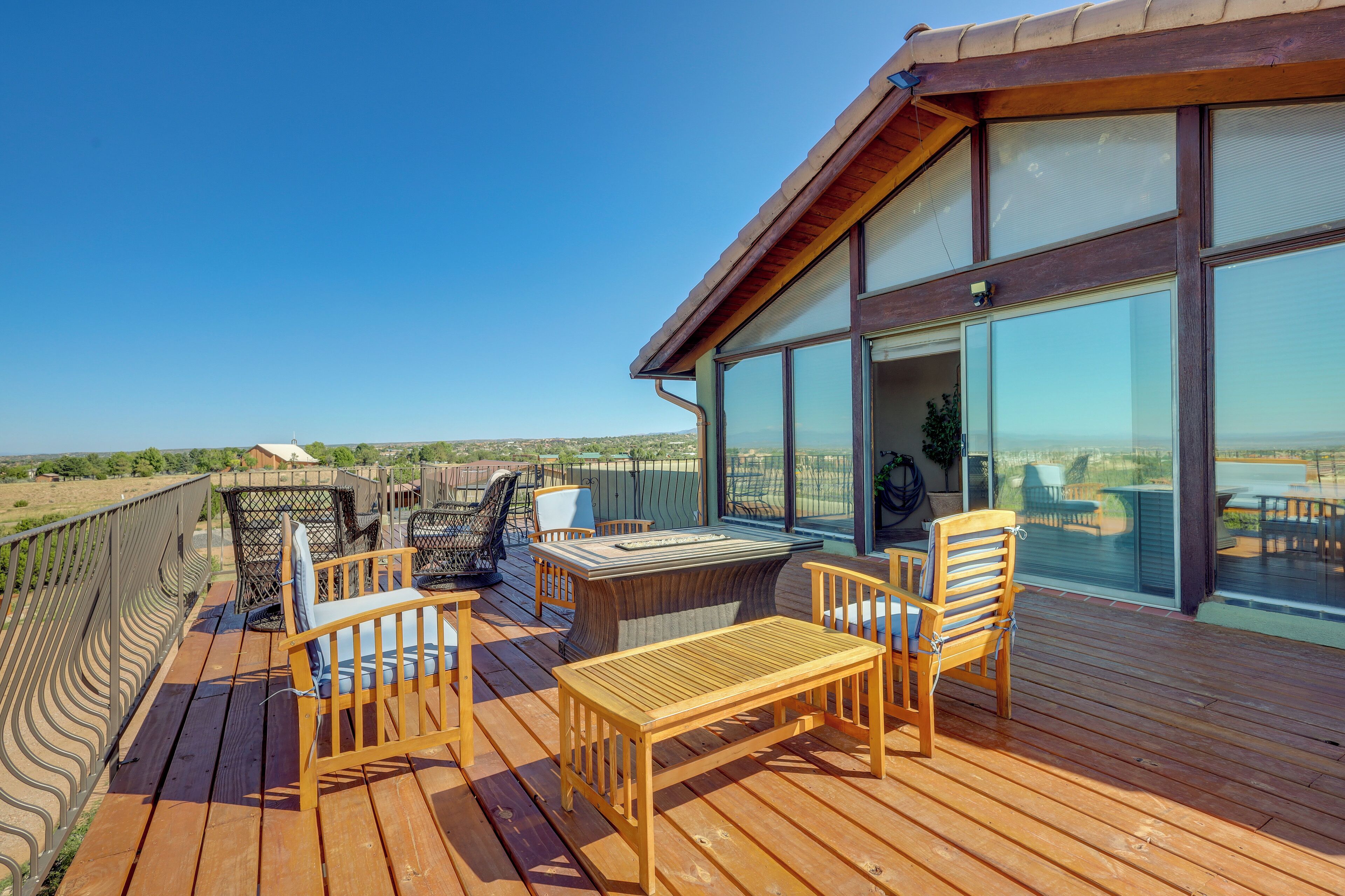 A wooden deck with outdoor furniture, large windows, and a view of the landscape.