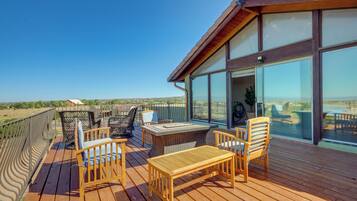 A wooden deck with outdoor furniture, large windows, and a view of the landscape.