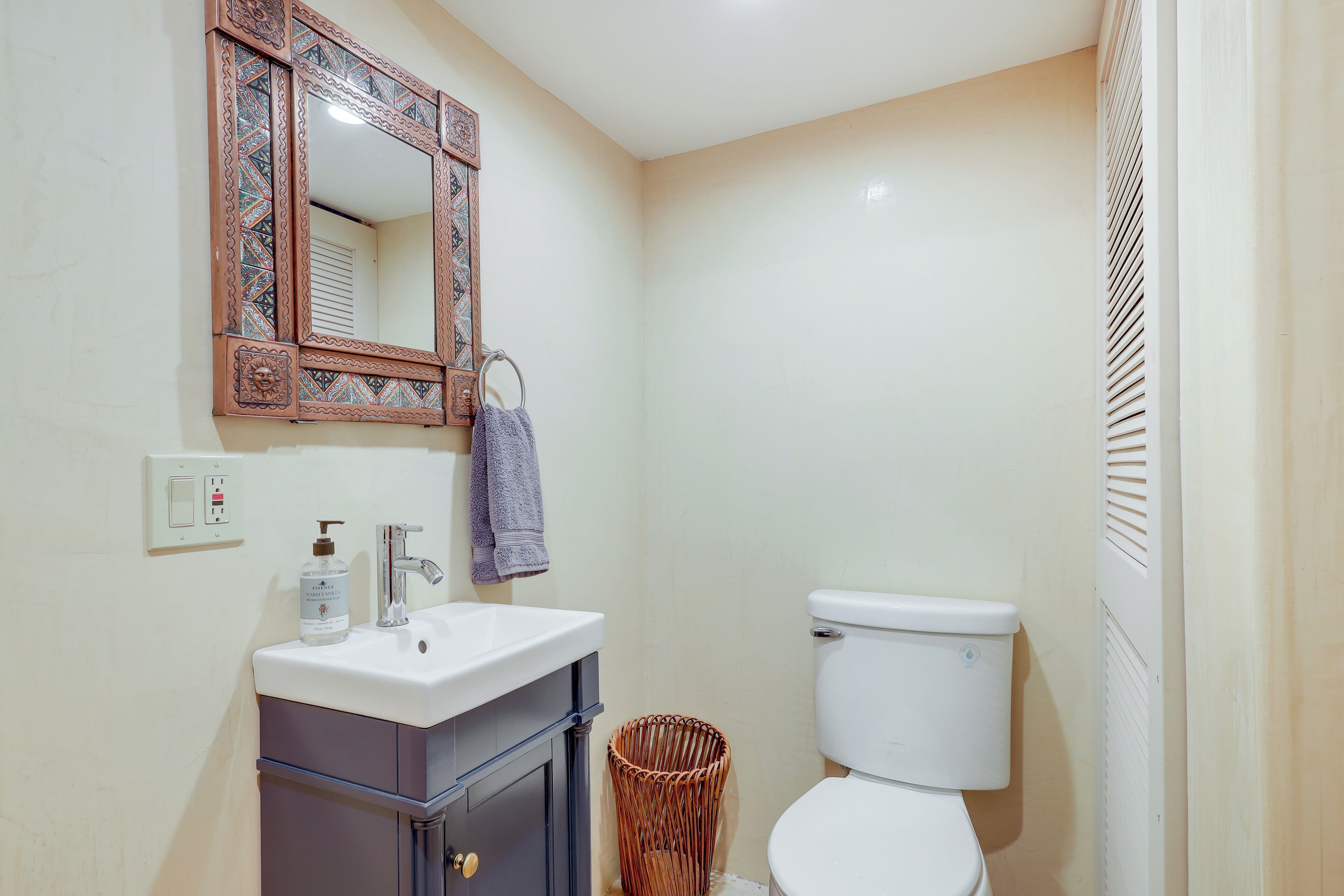 Un bagno con un WC bianco, un lavabo con uno specchio sopra e un asciugamano appeso al muro, oltre a un cestino.