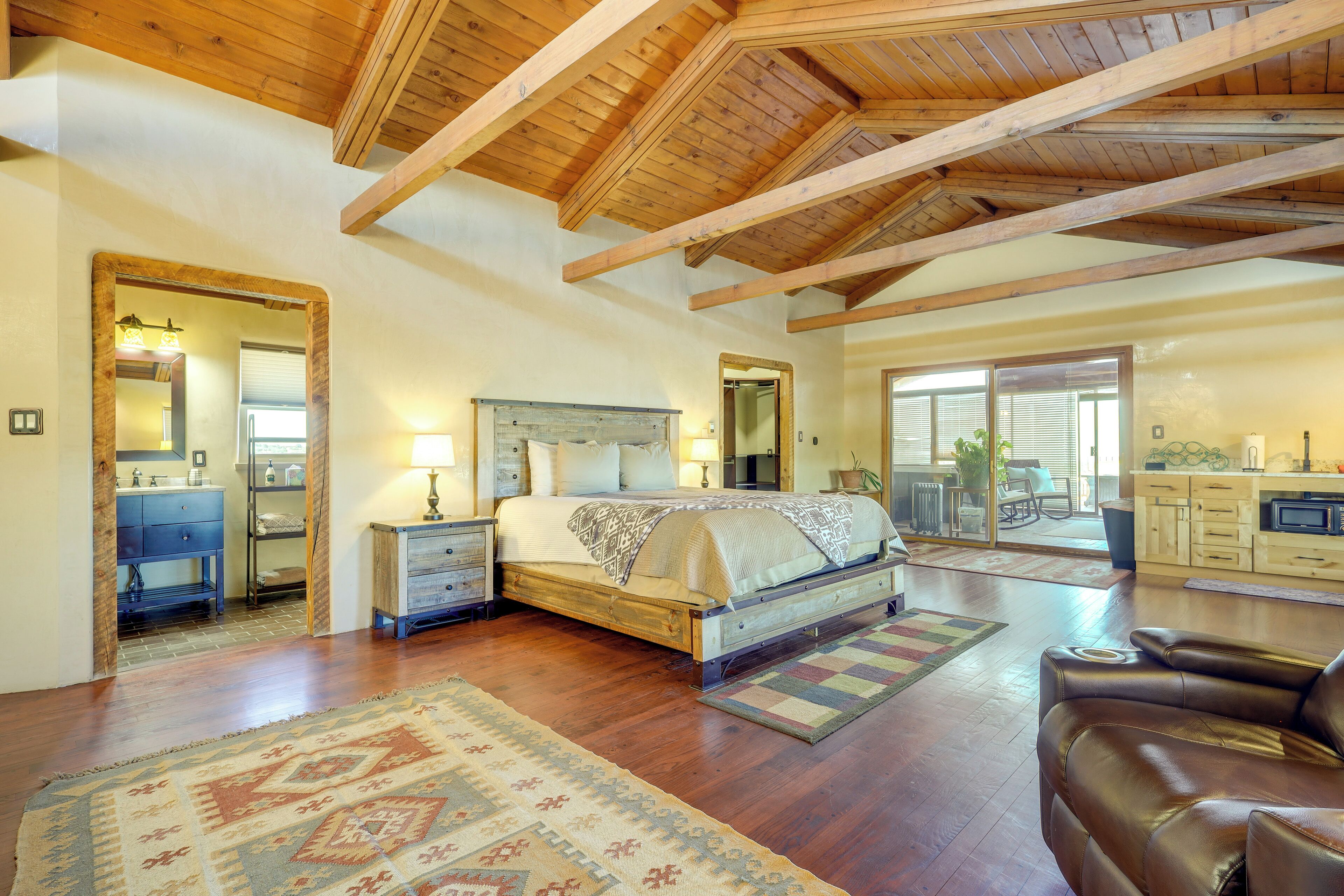 A spacious bedroom with a large bed, wooden ceiling beams, and a view to a patio area.