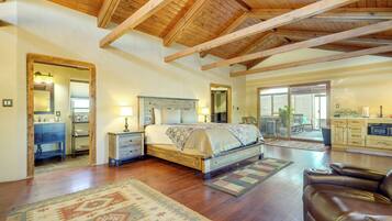 A spacious bedroom with a large bed, wooden ceiling beams, and a view to a patio area.