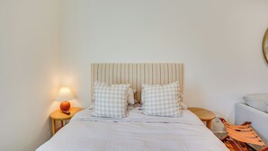 A neatly made bed with checkered pillows, a bedside lamp, and a small round table with a chair. - Modern Studio in Bend ~ 3 Mi to Sunriver Resort! (Bend)