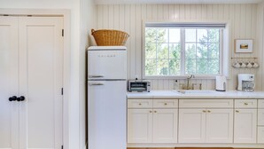 A kitchen with white cabinetry, a white refrigerator, a window with a view of trees, and a coffee maker. - Modern Studio in Bend ~ 3 Mi to Sunriver Resort! (Bend)