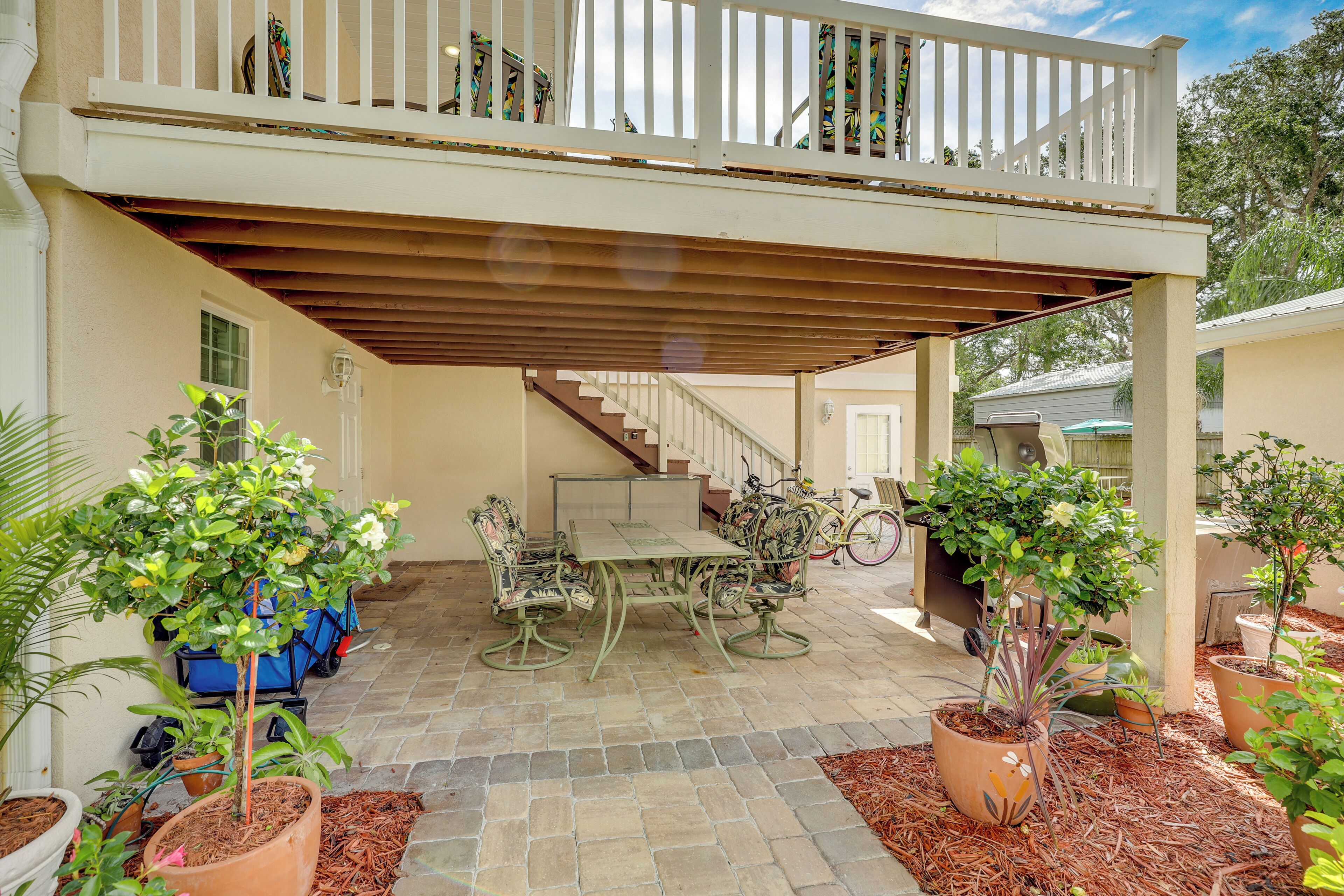 A covered patio with a table and chairs, surrounded by potted plants and a bicycle.