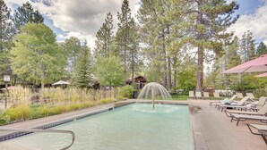 Une piscine dotée d’une fontaine, entourée de chaises longues et bordée d’une zone boisée.