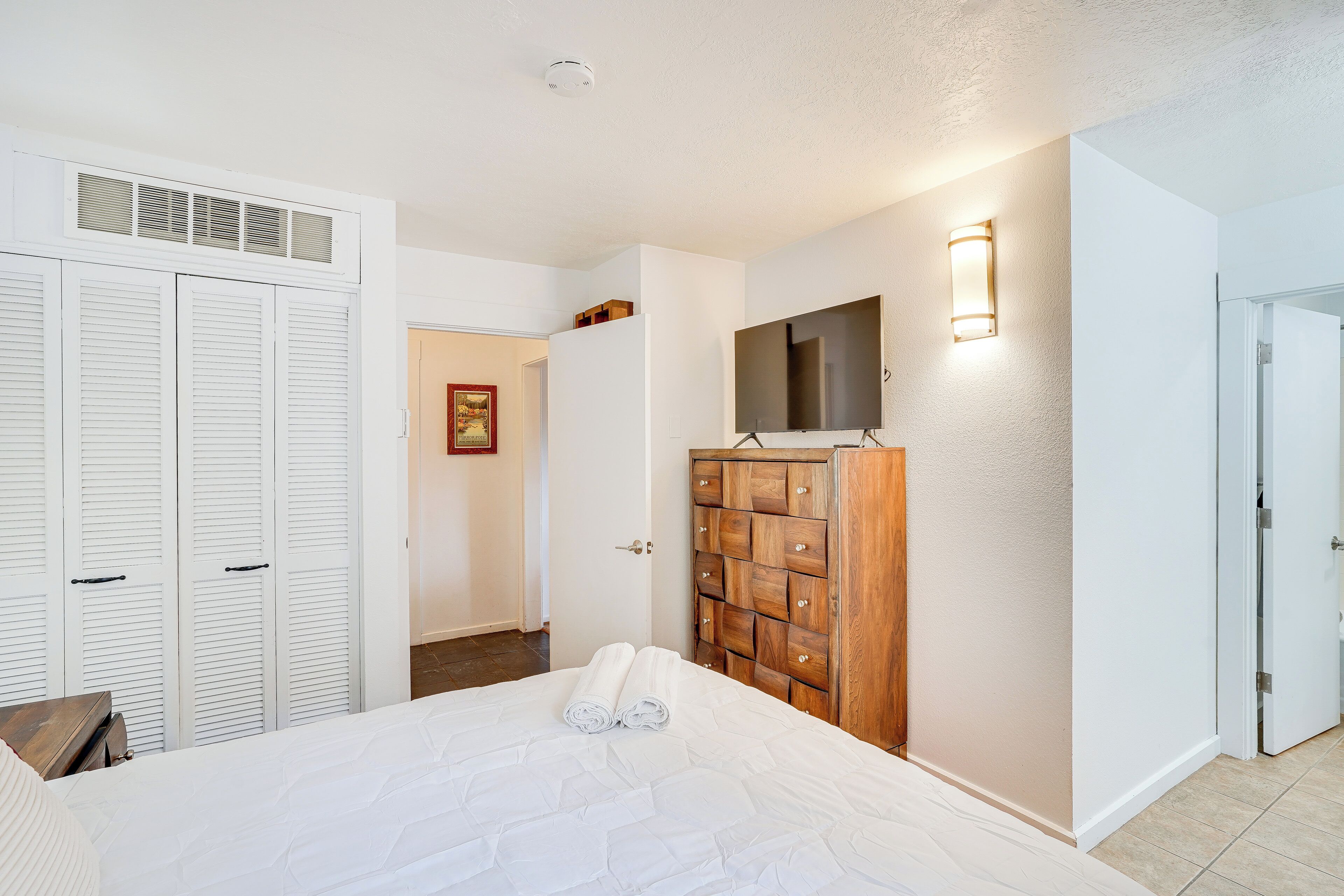 A bedroom with a bed, white closet, wooden dresser, and a wall-mounted TV.