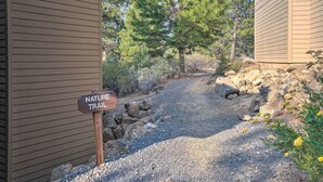 Un sentier de gravier mène à un panneau indiquant le début d’un sentier de découverte de la nature, le tout étant entouré d’arbres et de rochers.