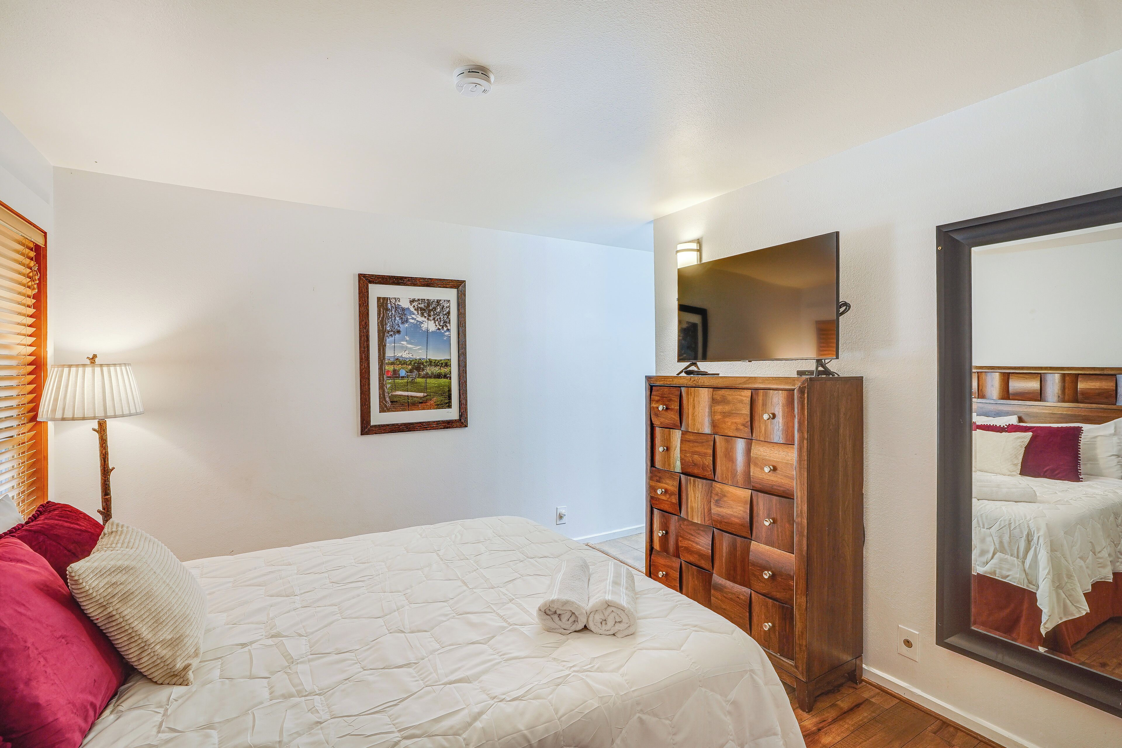 A bedroom with a bed, a dresser, a mirror, and a wall-mounted picture.