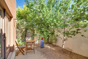 An outdoor patio with a wooden table and chairs, surrounded by trees and a potted plant. - Pet-friendly Albuquerque Vacation Escape! (Albuquerque)