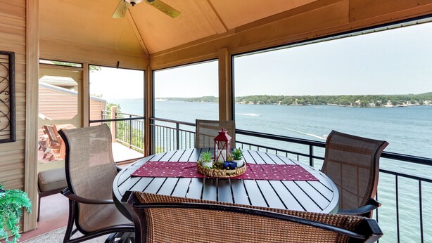 A covered outdoor area with a table and chairs, a ceiling fan, and a view of a body of water. - Pool Access + Views: Waterfront Lake Ozark Escape (Lake Ozark)